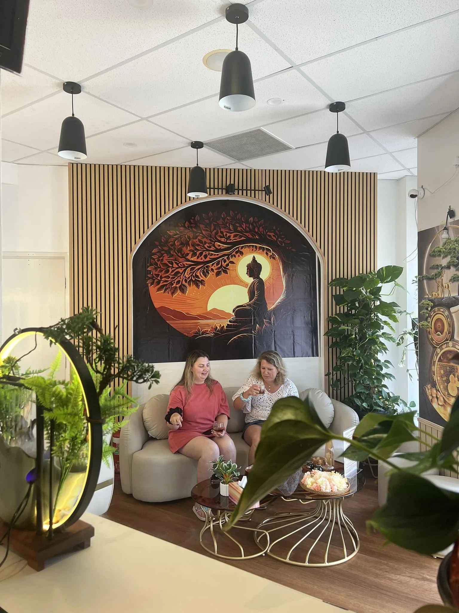Two women guests sharing tea on the cream sofa beneath the sunrise mural