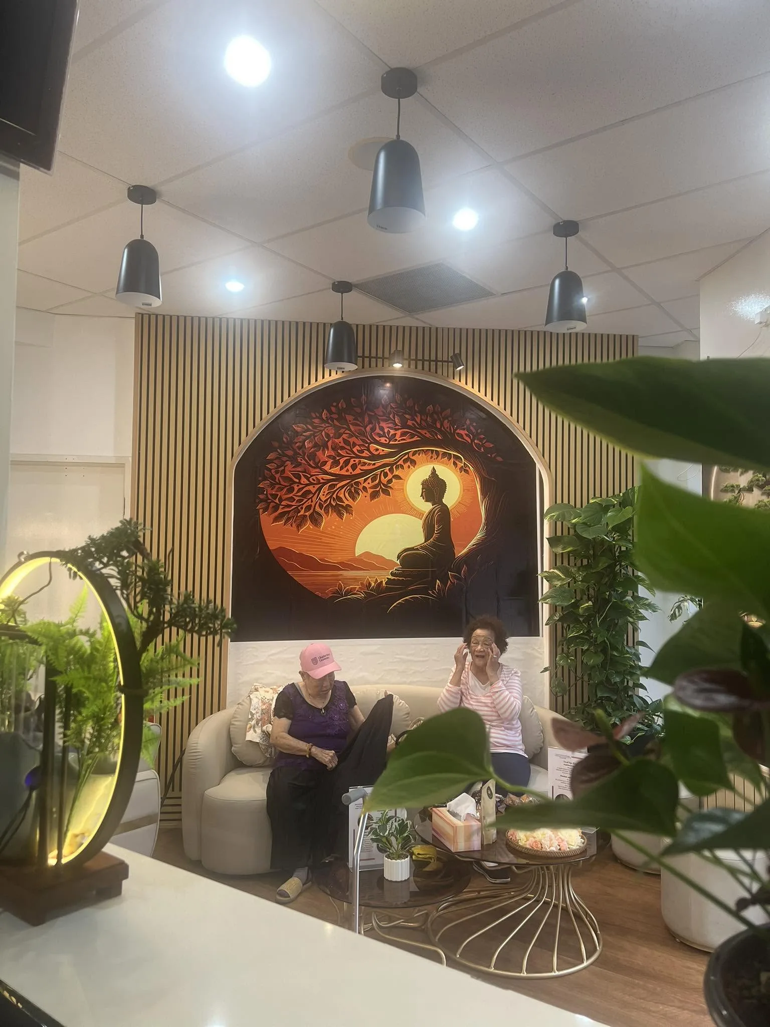 Two guests relaxing in the lounge — warm wood-slat walls and moon-gate mirror
