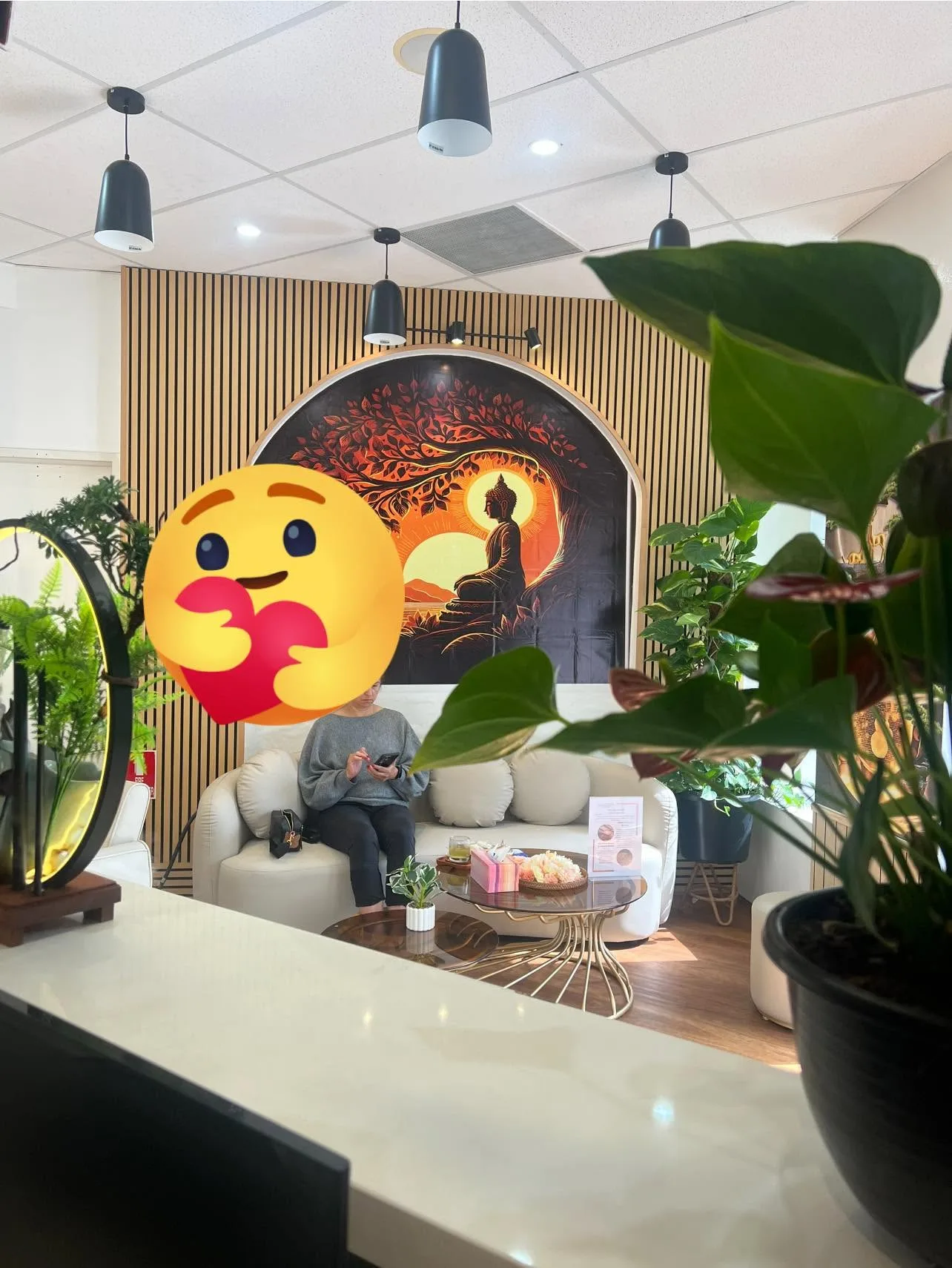 Guest on cream sofa beneath the mural — the lounge, moon-gate mirror and ferns (social post with emoji overlay)