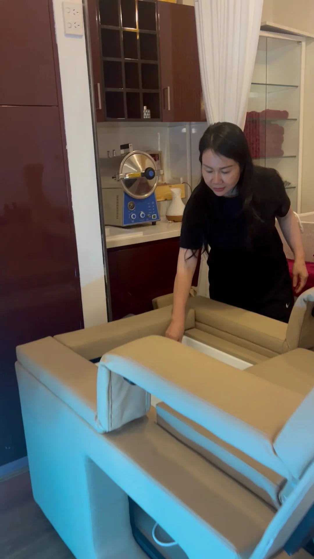A member of the team setting a head-spa recliner headrest, autoclave steriliser visible on the bench behind, towel cabinet to the right